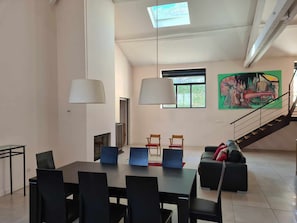 Un espace de salle à manger moderne, avec une grande table et des chaises, un escalier et un tableau coloré accroché au mur.