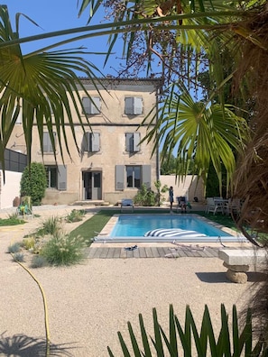 A pool with a wooden deck, a building with shutters, and palm trees. - Holiday Home “La Maison des Remparts” with Private Pool, Wi-Fi & Air Conditioning (Clérieux)