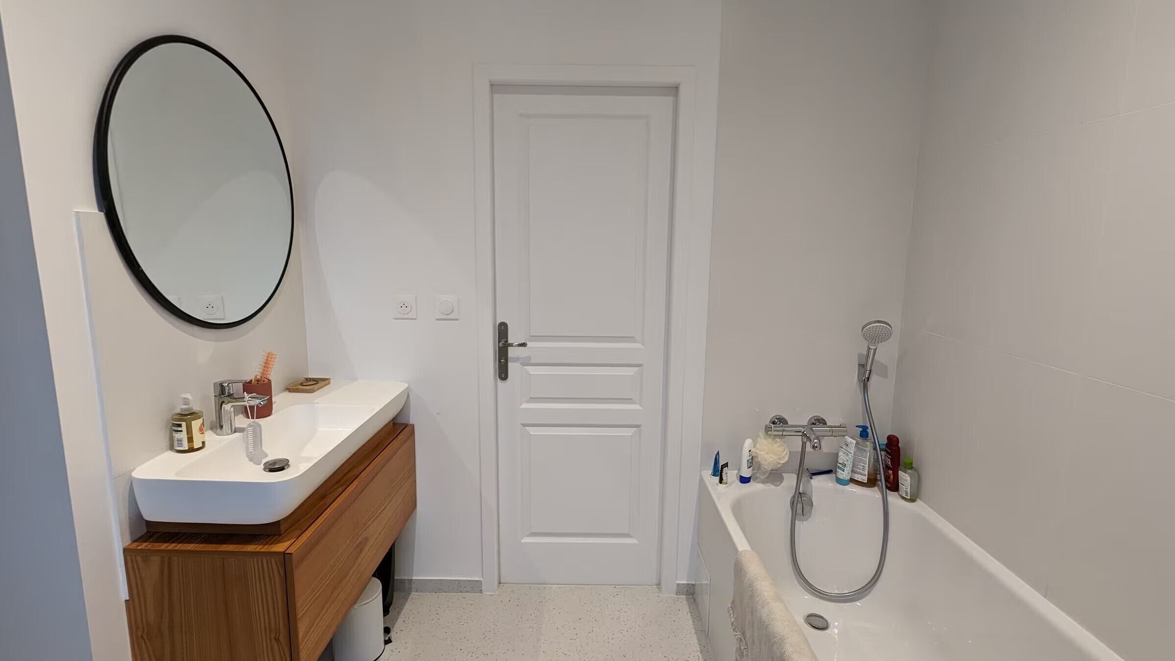 Un baño con lavamanos blanco, espejo, puerta y ducha.