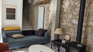 A living room with a stone wall, a black stove, a sofa, a coffee table, and a chair. - La Maison des Remparts: Private Pool, Wi-Fi, Air Conditioning – Holiday Home in Clérieux (Clérieux)