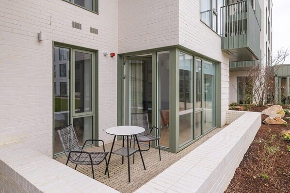 A modern building with a glass door entrance, a small patio with a table and chairs, and a brick pathway. - Apex Executive Apartments - The Lookout (Dublin)