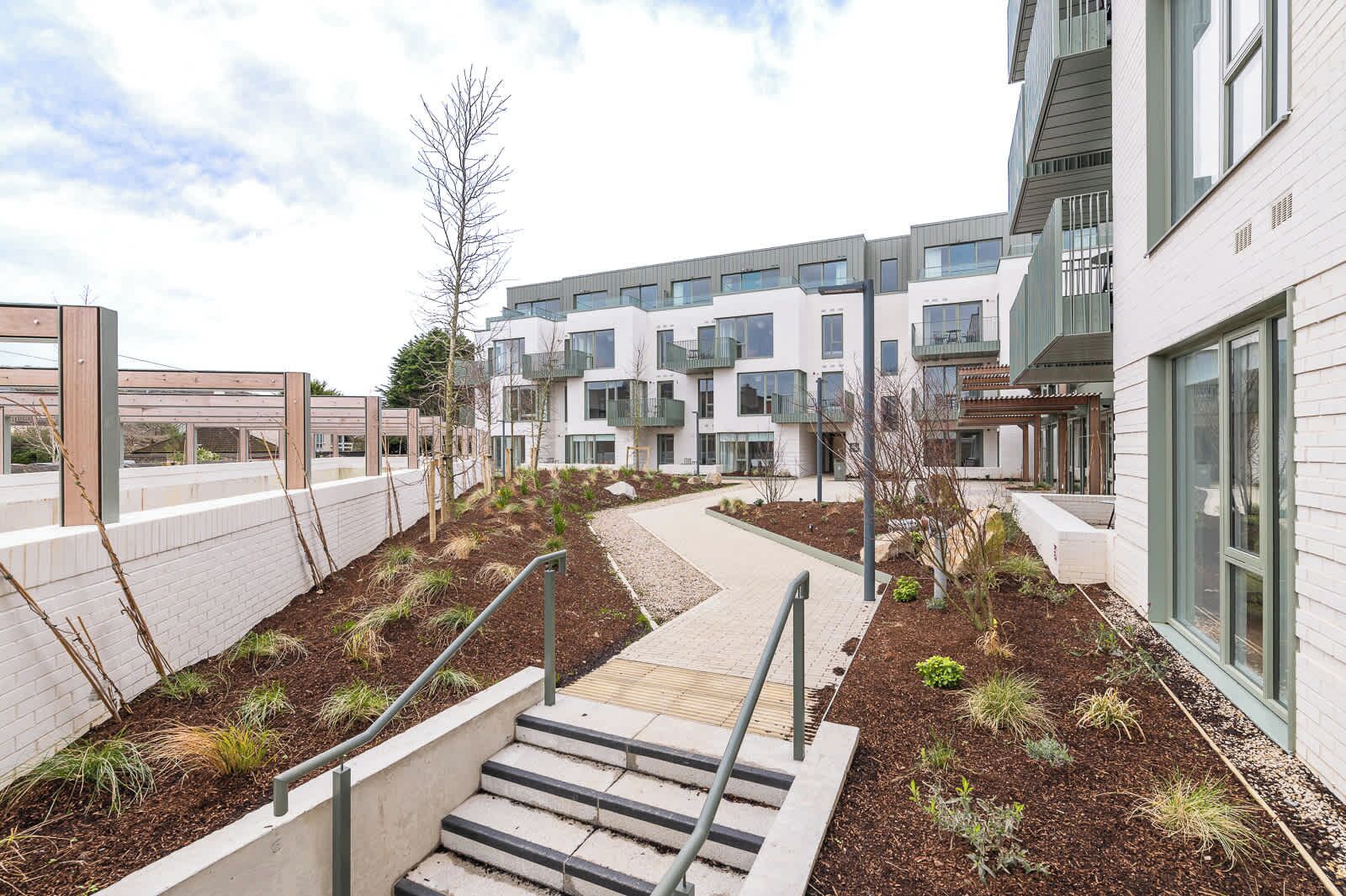 A modern building with a central pathway, steps leading to a lower level, and a landscaped area with plants.