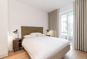 A modern bedroom with a large bed, two bedside tables with lamps, a wooden headboard, and a large window with curtains. - Apex Executive Apartments - The Lookout (Dublin)