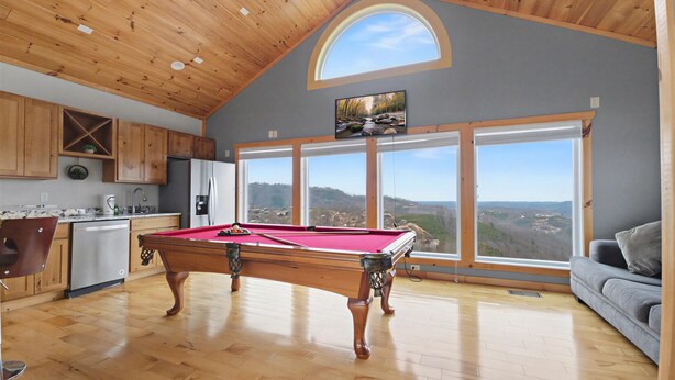Une pièce spacieuse équipée d’une table de billard, de meubles en bois et de grandes fenêtres donnant sur la campagne.