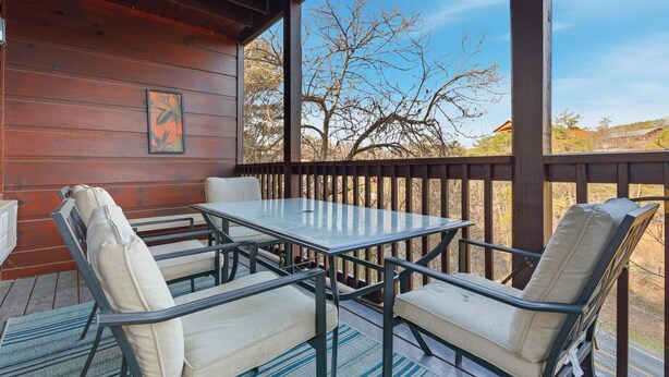 Un espacio al aire libre techado con una mesa y sillas, barandas de madera y vistas a árboles y colinas.