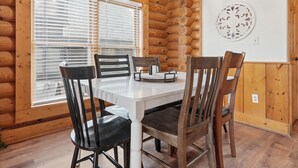 Interior de una cabaña de troncos con una mesa de comedor, cuatro sillas y un adorno en la pared.