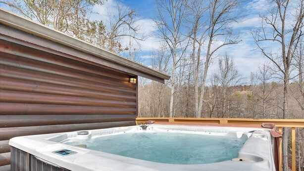 A hot tub on a wooden deck with a view of trees and a building in the background. - A Family Affair #712 (Gatlinburg)