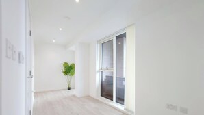 A room with a large window, a potted plant, and a light-colored floor. - Deluxe Serviced Three Bedroom Apartment (London)