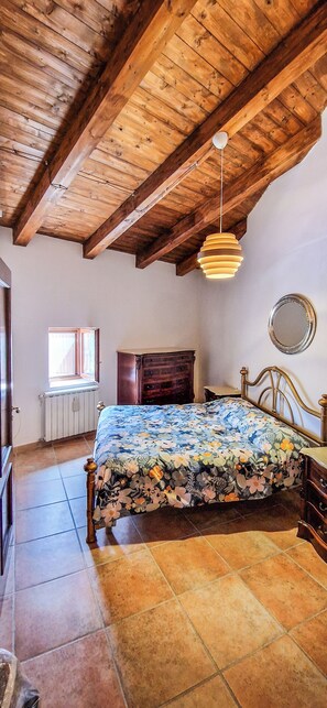 Un dormitorio con techo de madera, cama con colcha floral, cómoda, espejo y ventana con vistas.