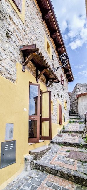 Un bĂątiment en pierre avec une façade jaune, une porte en bois et une petite fenĂȘtre.
