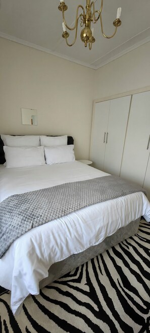 Ein Schlafzimmer mit einem Bett, einem zebra-gemusterten Teppich, einem weißen Kleiderschrank und einer Chandelüster.