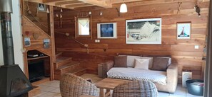 A wooden cabin interior with a sofa, wicker chairs, a fireplace, and framed artwork on the walls. - 104m² wooden chalet in the heart of a preserved regional mountain park (Molines en Queyras)