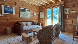 Interno di una baita in legno con un divano, una poltrona in vimini e un tavolo da pranzo.