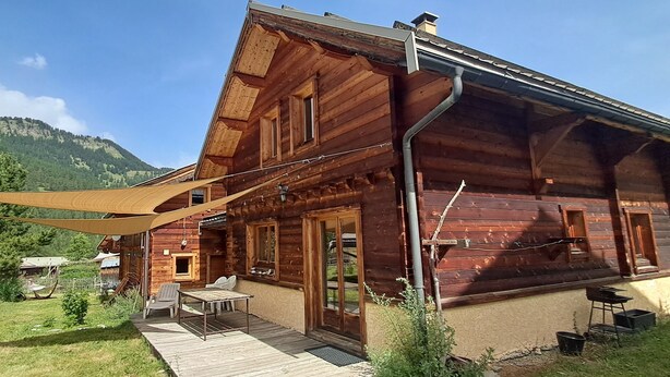 Un chalet in legno con una terrazza, posti a sedere all'aperto e vista sulle montagne.