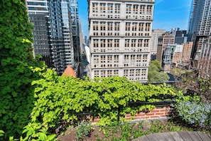 A cityscape with modern buildings, a brick wall with green foliage, and a clear blue sky. - 17John: Deluxe 1 Bed W/D in unit + GYM + Lounge (New York)