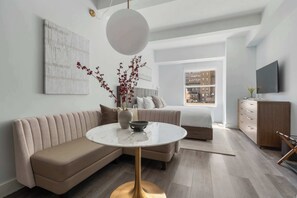 Ein modernes Wohnzimmer mit einer Couch, einem runden Couchtisch, einem Bett, einem Fernseher und Blick auf die Stadt.