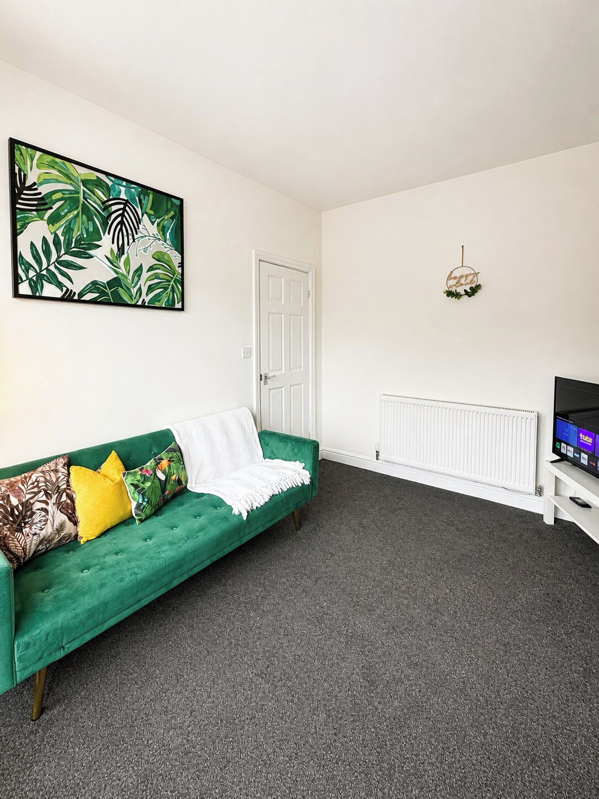 A room with a green sofa, a white door, a radiator, and a TV on a stand.