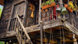 Una cabaña rústica de madera con balcón, barandillas de madera y macetas colgantes.