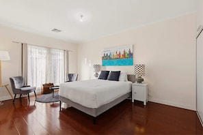 A hotel room with a large bed, two chairs, a desk, and a painting on the wall. - Beautiful 4 Bedroom Home Near Marion & Flinders (Seacombe Gardens)