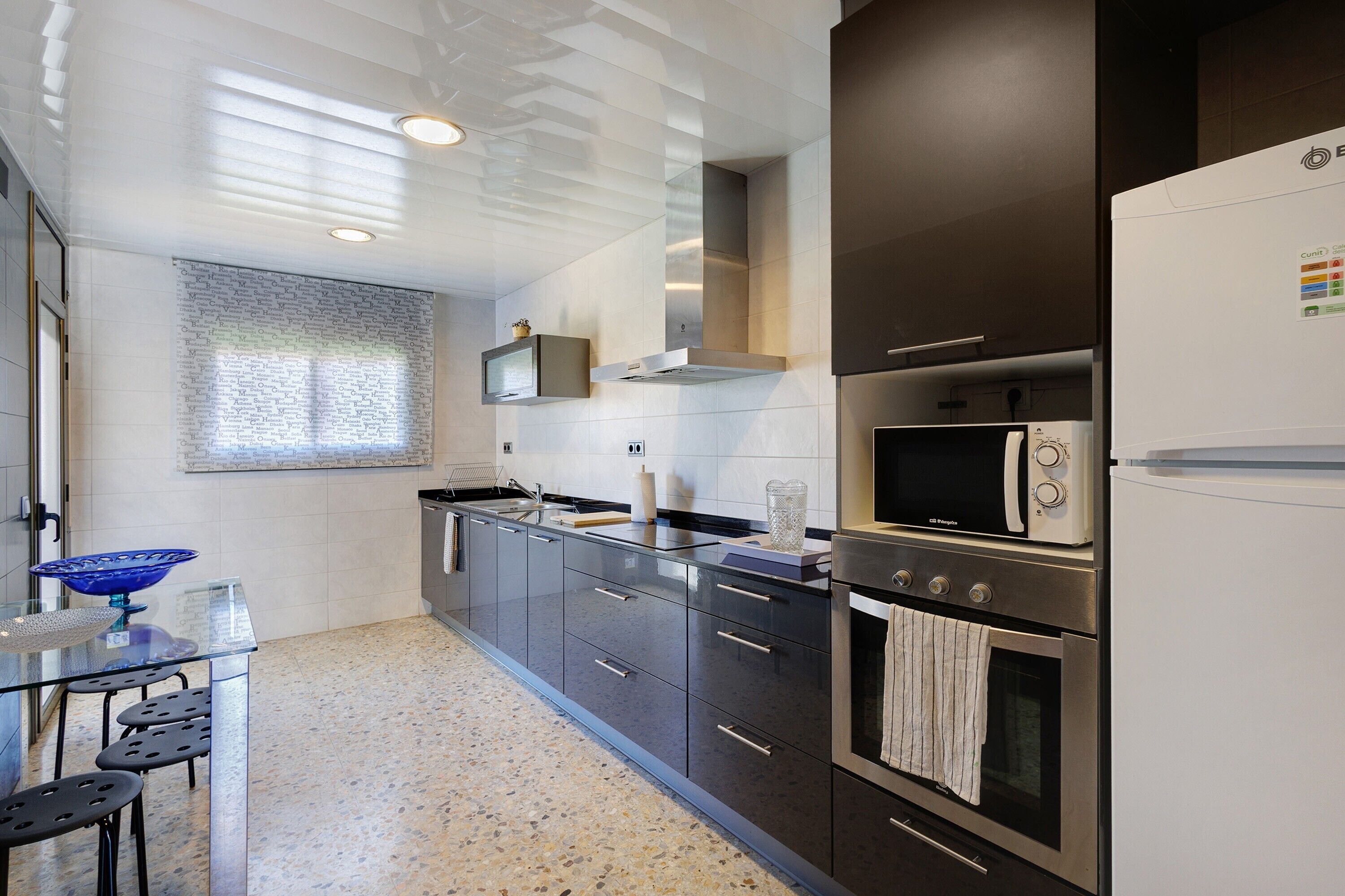 Una cocina moderna con mesa de vidrio, electrodomésticos de acero inoxidable y ventana con persianas.