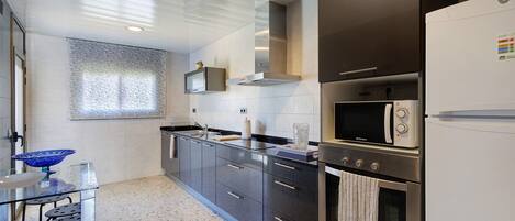 Una cocina moderna con mesa de vidrio, electrodomésticos de acero inoxidable y ventana con persianas.