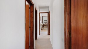 A hallway with wooden doors, a ceiling vent, and a table with chairs in the distance.