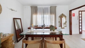 A dining area with a glass table, wooden chairs, a vase, and a mirror on the wall.