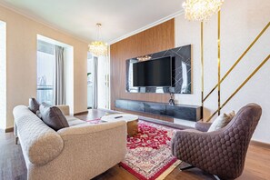 Ein modernes Wohnzimmer mit großem Flachbildfernseher, einem beige-farbenen Sofa, einem gemusterten Teppich und einer Wand mit Holzpaneelen.