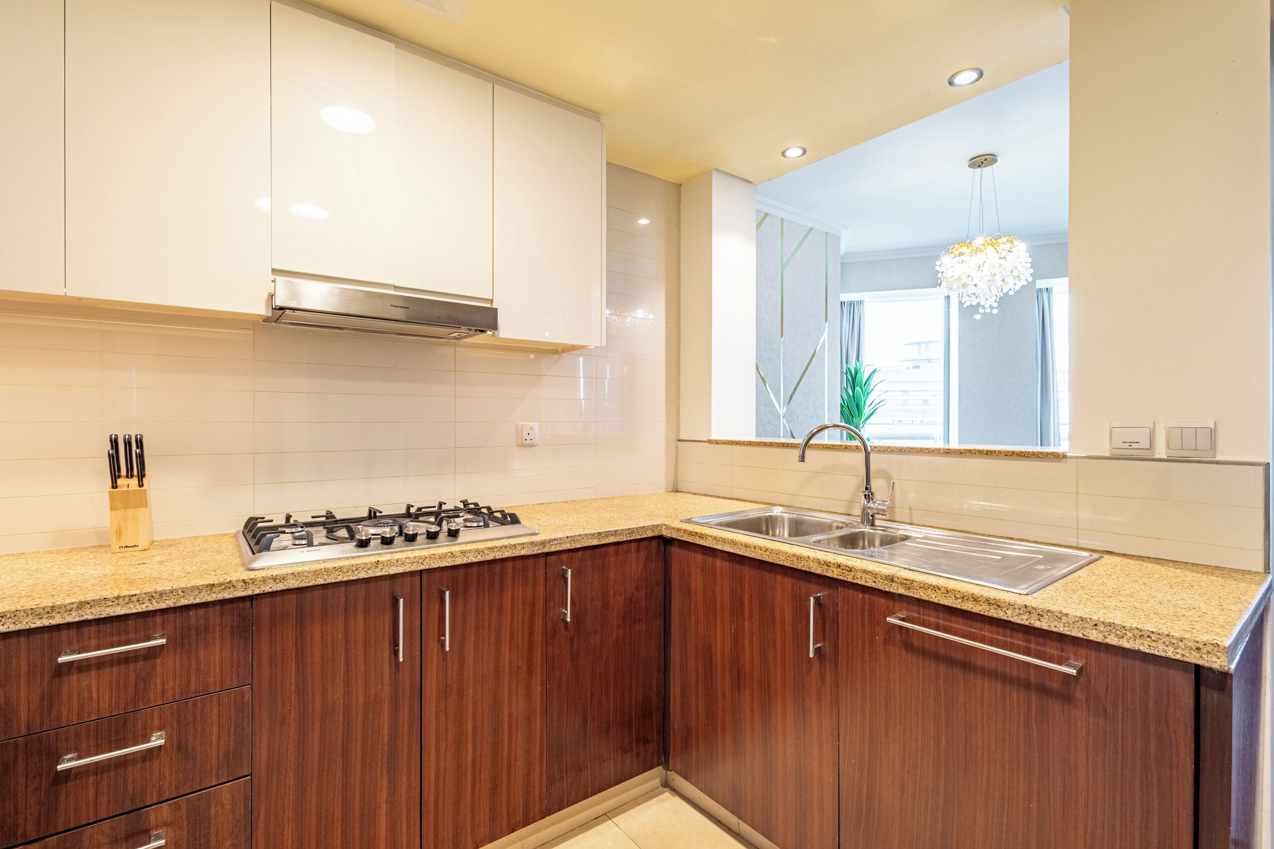 A modern kitchen with wooden cabinets, a gas stove, a stainless steel sink, and a pendant light.