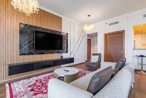 Ein modernes Wohnzimmer mit großem Flachbildfernseher, einer Couch, einem Couchtisch und einer Deckenleuchte.
