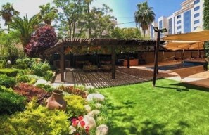 Un giardino con una pergola, posti a sedere all'aperto e una piscina.