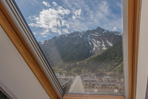 Blick durch ein Fenster auf eine Berglandschaft mit schneebedeckten Gipfeln und einer Stadt darunter.