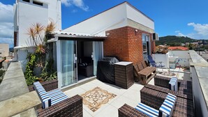 A rooftop patio with outdoor furniture, a sliding glass door, and a brick wall. - Penthouse with terrace (Florianópolis)