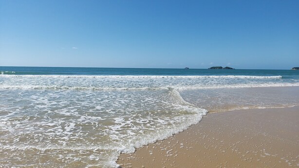 A beach with waves, a clear sky, and distant islands. - Penthouse with terrace (Florianópolis)