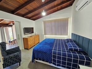 A bedroom with a wooden ceiling, a bed with a blue and white checkered bedspread, a television on a wooden dresser, and a window with blinds. - Penthouse with terrace (Florianópolis)