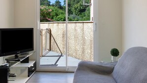 Un salon équipé d’un téléviseur à écran plat, d’un canapé, d’une petite table avec une plante et d’une porte-fenêtre coulissante donnant sur un balcon extérieur.