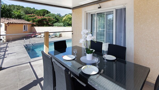 Une table de salle à manger avec un plateau en verre, des chaises, une piscine et une vue sur une maison et des arbres.