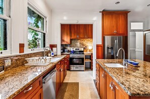 Eine moderne Küche mit Granitarbeitsplatten, Edelstahlgeräten, Holzausbau und einem großen Fenster.