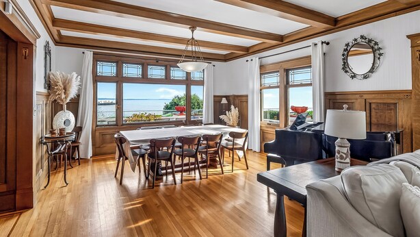 Ein großzügiger Essbereich mit Holztisch und Stühlen, große Fenster mit Meerblick und eine gemütliche Sitzecke mit Sofa und Lampe.
