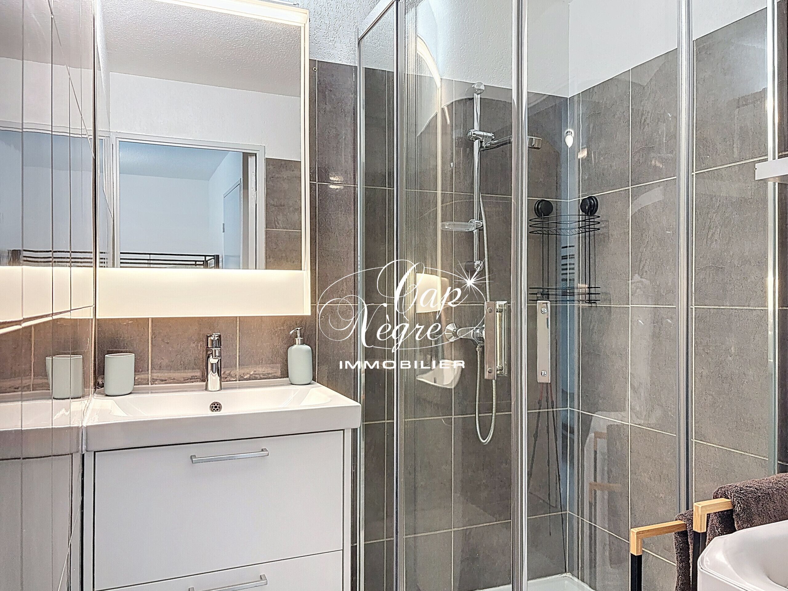 Un baño moderno con cabina de ducha de vidrio, tocador con espejo y perchero para toallas.