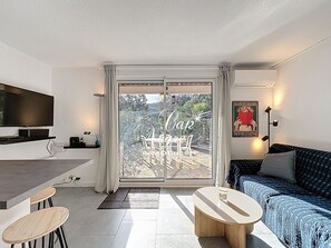 A modern living room with a flat-screen TV, a dining area with chairs, a sofa, and a coffee table. - Charming T2 cabin for 4 people renovated with garden, pool and beach walk to Cavalière (Le Lavandou)