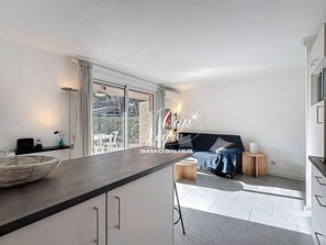 A modern kitchen with a large island, sliding glass doors to a patio, and a cozy seating area with a sofa and side tables. - Charming T2 cabin for 4 people renovated with garden, pool and beach walk to Cavalière (Le Lavandou)