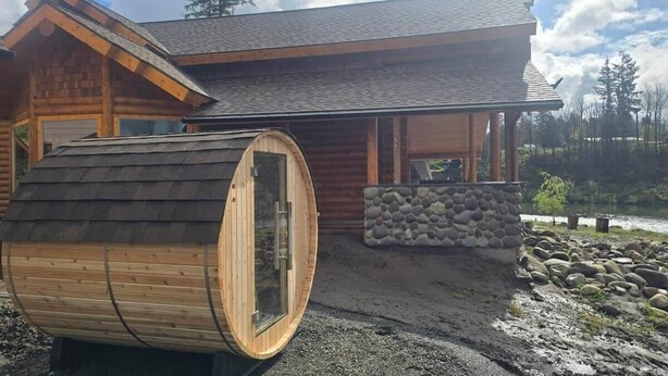 A wooden cabin with a sauna, stone wall, and a view of a lake. - Tranquil River Front log cabin retreat (Gates)