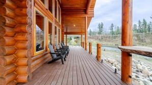 A wooden log cabin with a deck, outdoor seating, and a view of a river. - Tranquil River Front log cabin retreat (Gates)