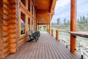 A wooden log cabin with a deck, outdoor seating, and a view of a river. - Tranquil River Front log cabin retreat (Gates)