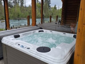 A hot tub with a wooden deck and a river view.