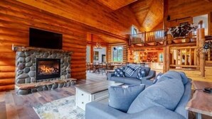 A log cabin interior with a stone fireplace, a sofa, and a dining area. - Tranquil River Front log cabin retreat (Gates)