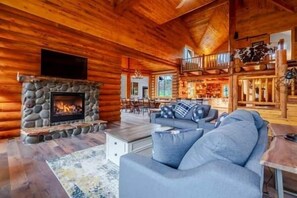A log cabin interior with a stone fireplace, a sofa, and a dining area. - Tranquil River Front log cabin retreat (Gates)