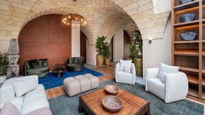A spacious lounge area with a stone arch ceiling, a wooden coffee table, and seating arrangements including sofas and armchairs. - MBH | Laguna King Suite (Diso Spongano)