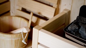 A sauna room with a wooden bench, a wooden bucket, and a tray with stones. - MBH | Laguna King Suite (Diso Spongano)